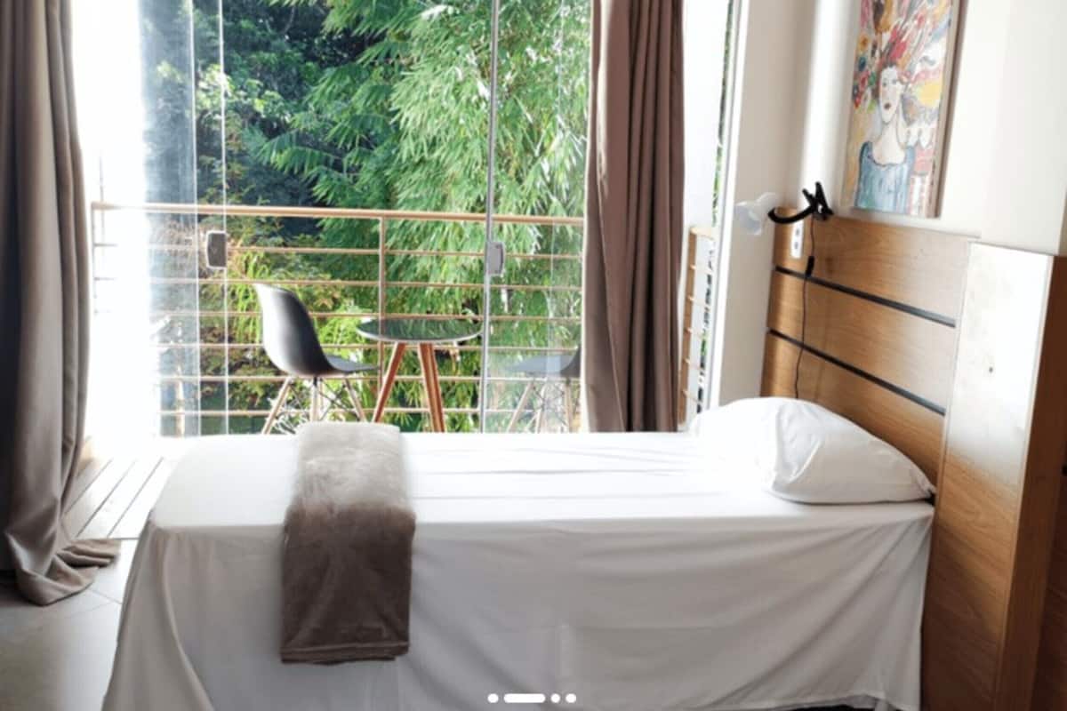 Une chambre d’hôtel avec un lit, une chaise et une vue sur la verdure par la fenêtre.