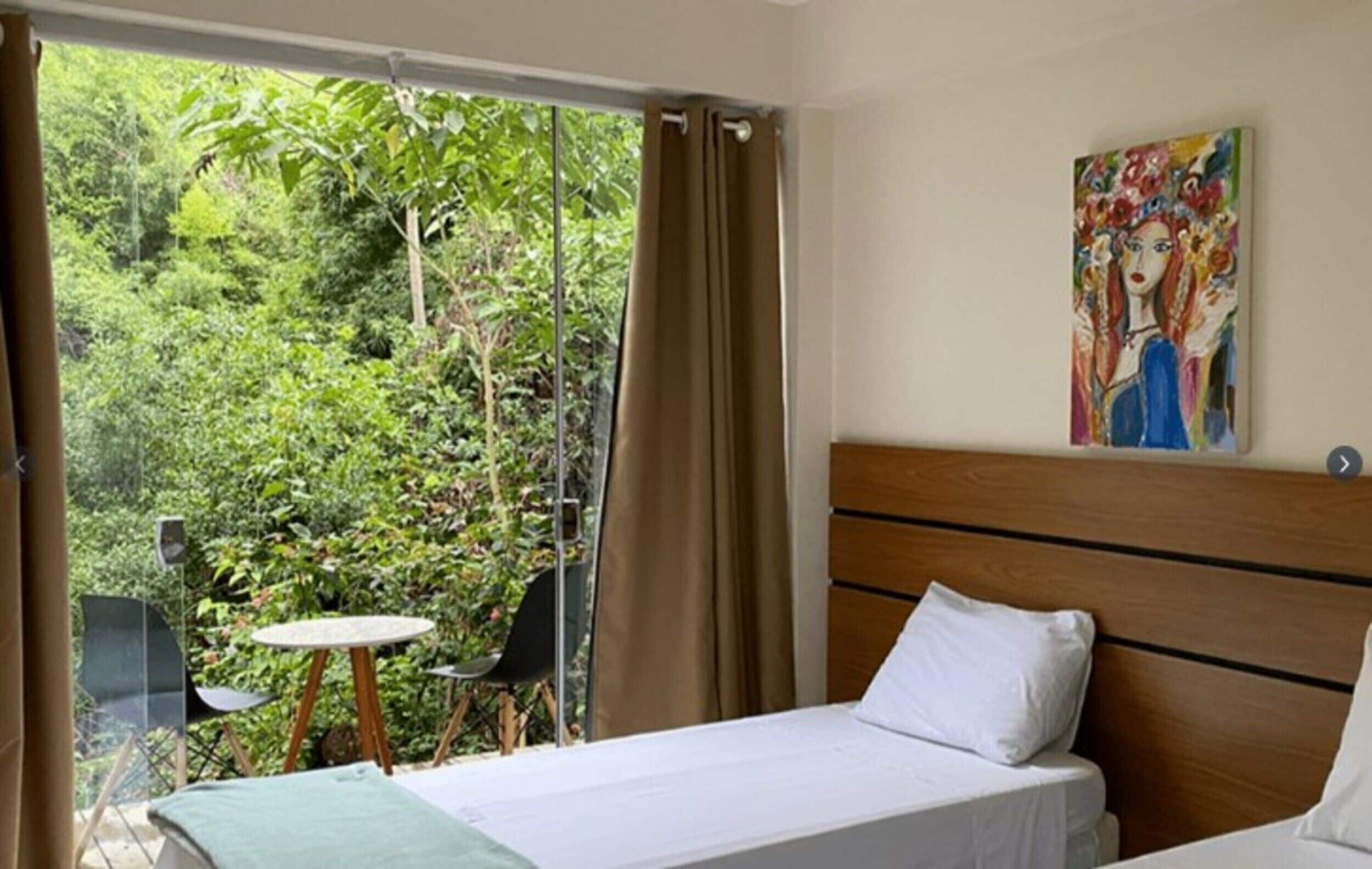 Habitación de hotel con cama, una mesita, sillas, cortinas en la ventana y un cuadro en la pared.