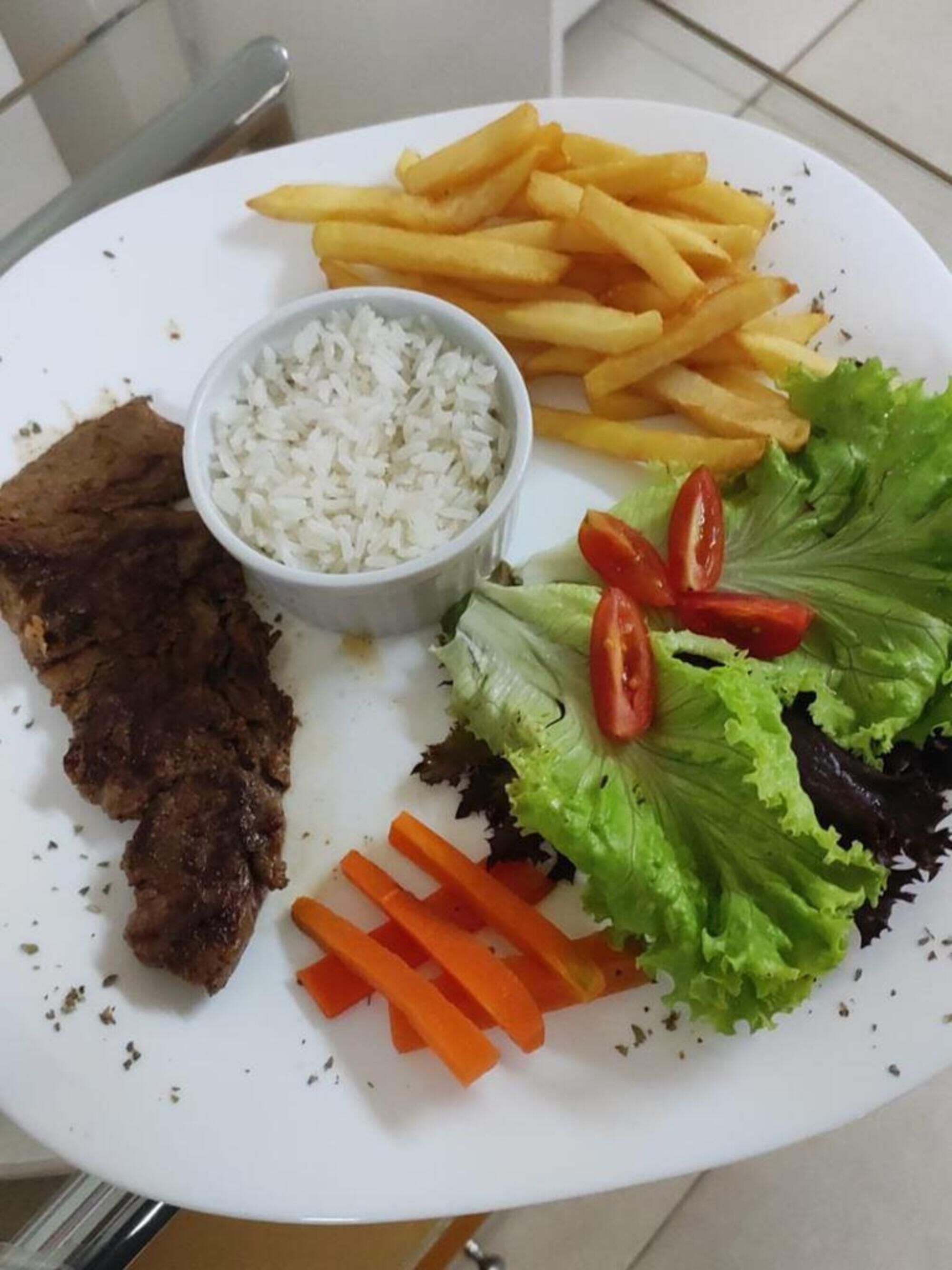 A plate with steak, French fries, rice, lettuce, and carrot sticks.