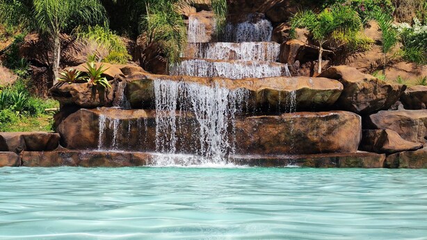 Una piscina turquesa y cristalina con una cascada que se desliza entre rocas y abundante vegetación.