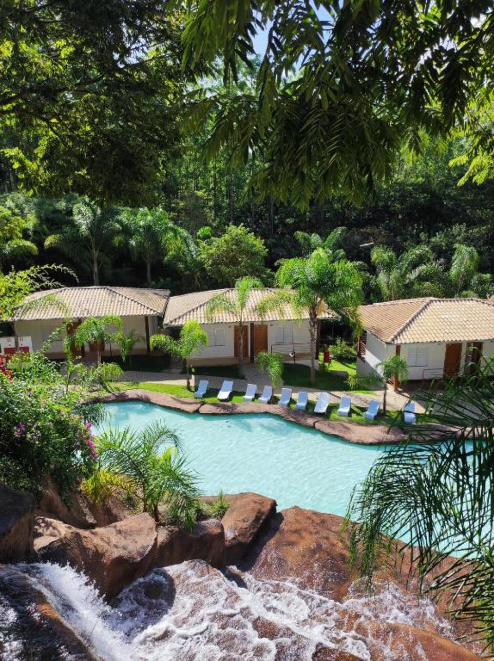 Resort com piscina, cadeiras de descanso e cachoeira.