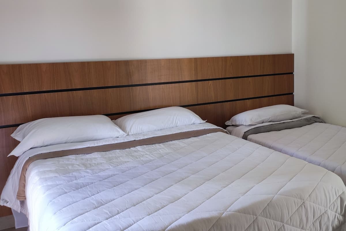 Un lit double avec une tête de lit en bois et deux draps blancs.