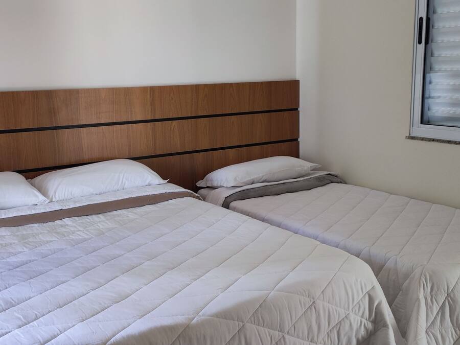 Una cama doble con cabecera de madera y dos sábanas blancas.