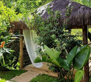 A thatched-roof structure surrounded by lush greenery and a variety of plants. - Hotel Serra do Gandarela (Rio Acima)