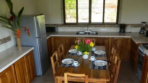 Une cuisine avec des meubles en bois, un réfrigérateur en acier inoxydable, une table à manger dressée avec des assiettes, des tasses et un vase rempli de fleurs.