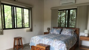 Une chambre à coucher avec un lit en bois, une table de chevet, un petit tabouret et une commode décorative en bois.