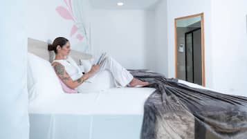 Una persona sentada en una cama en una habitación con pared blanca y una puerta.