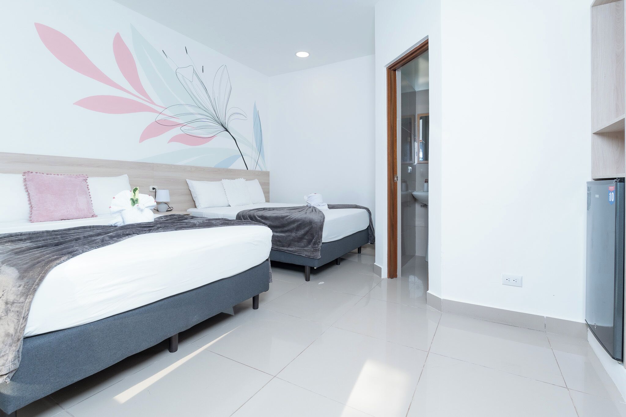 Una habitación de hotel moderna con dos camas, un cuadro de flores grande en la pared y una puerta de cristal que da al baño.