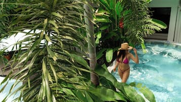 Mulher de biquíni e chapéu perto de uma piscina, rodeada por plantas tropicais.