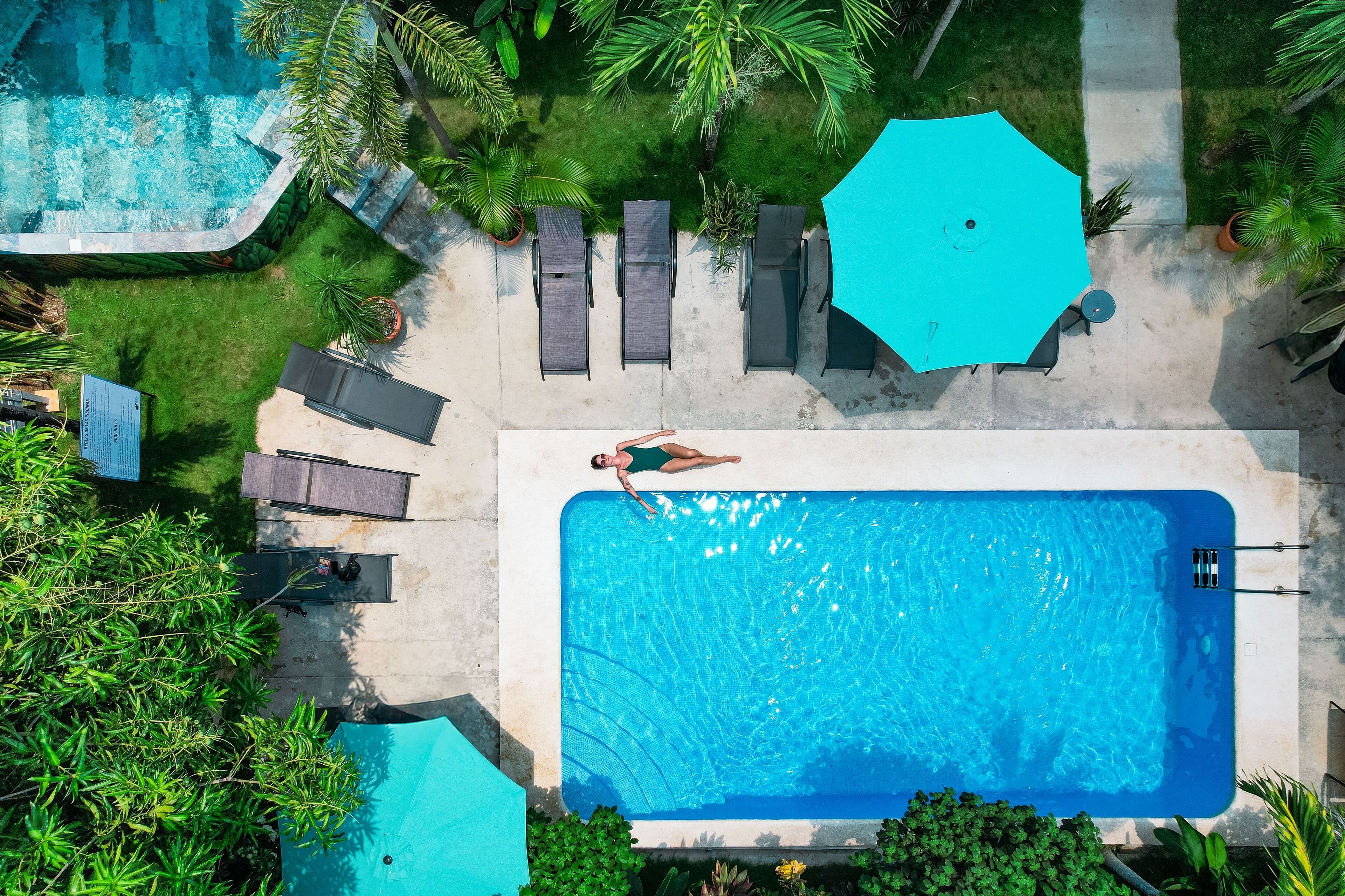 An aerial view of a swimming pool area with lounge chairs, a large umbrella, and surrounding greenery.