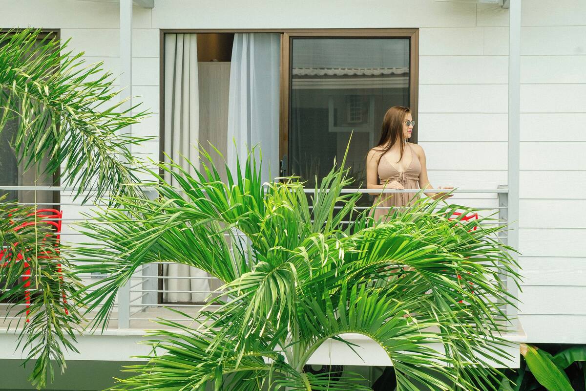 A balcony with a person, a white building, and green plants.