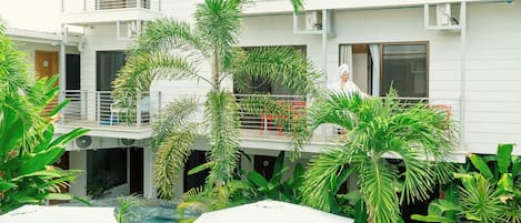 Un edificio a più piani con balconi, una piscina e rigogliosa vegetazione tropicale.