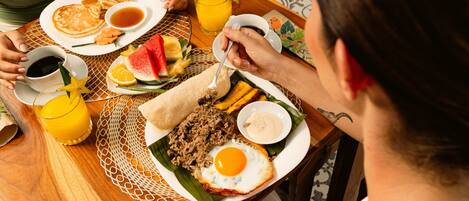 A dining table with plates of food, including pancakes, a fried egg, and a wrap, along with drinks and condiments.