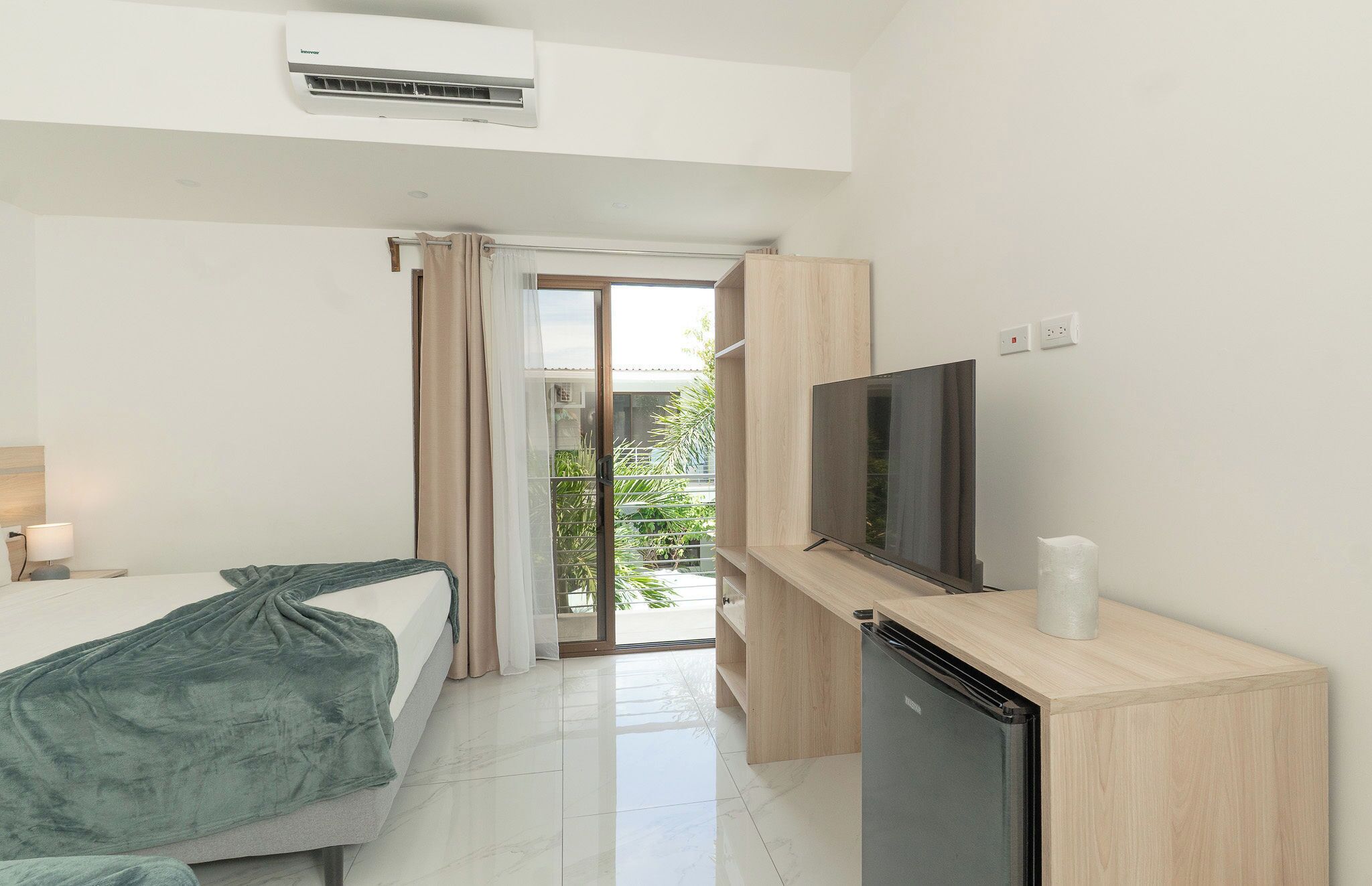 A hotel room with a bed, a TV, a refrigerator, and a balcony with a view.