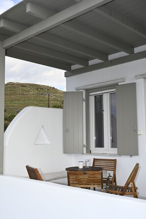 Un espace extérieur aménagé avec une table et des chaises, une fenêtre avec des volets et une vue sur une colline.