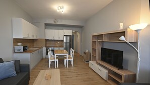 A modern apartment with a kitchen, dining area, and living room. It includes a sofa, a coffee table, a TV, and a lamp. - Τinos Deluxe Home (Τήνος)