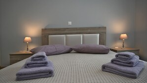 A neatly made bed with a textured bedspread, two pillows, and two folded towels. - Τinos Deluxe Home (Τήνος)