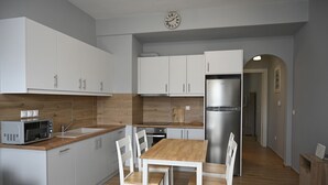 A modern kitchen with white cabinets, a wooden countertop, a stainless steel refrigerator, and a dining table with chairs. - Τinos Deluxe Home (Τήνος)