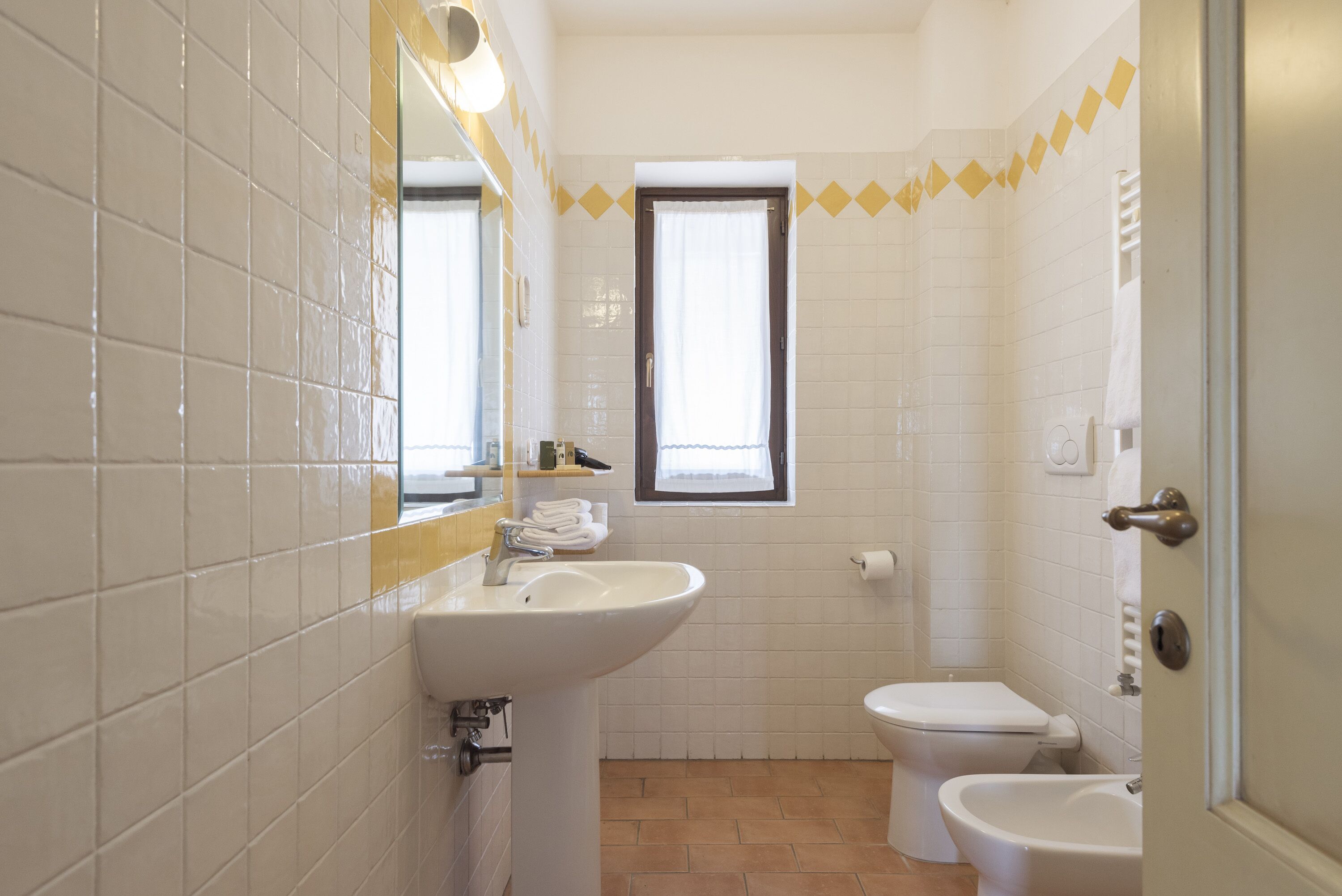 A bathroom with white tiles, a sink, a toilet, and a bidet.