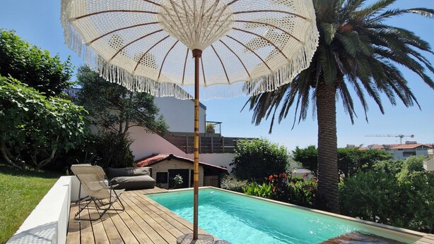 A poolside area with a wooden deck, a white umbrella, and a palm tree. - Very pretty 4* listed wooden house in Biarritz with swimming pool (Biarritz)
