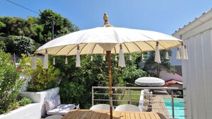 A wooden table with white chairs, a white umbrella, and a pool in the background. - Very pretty 4* listed wooden house in Biarritz with swimming pool (Biarritz)