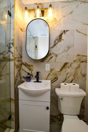 A bathroom with a marble wall, a white sink, a mirror, and a toilet.