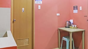 A small room with a wooden door, a table with a kettle and cups, a blue stool, and a mat at the door. - Solanos Transient House (Pasay)