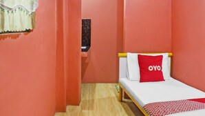 A small, narrow room with a single bed, a red pillow with "OYO" on it, and a wooden floor. - Solanos Transient House (Pasay)