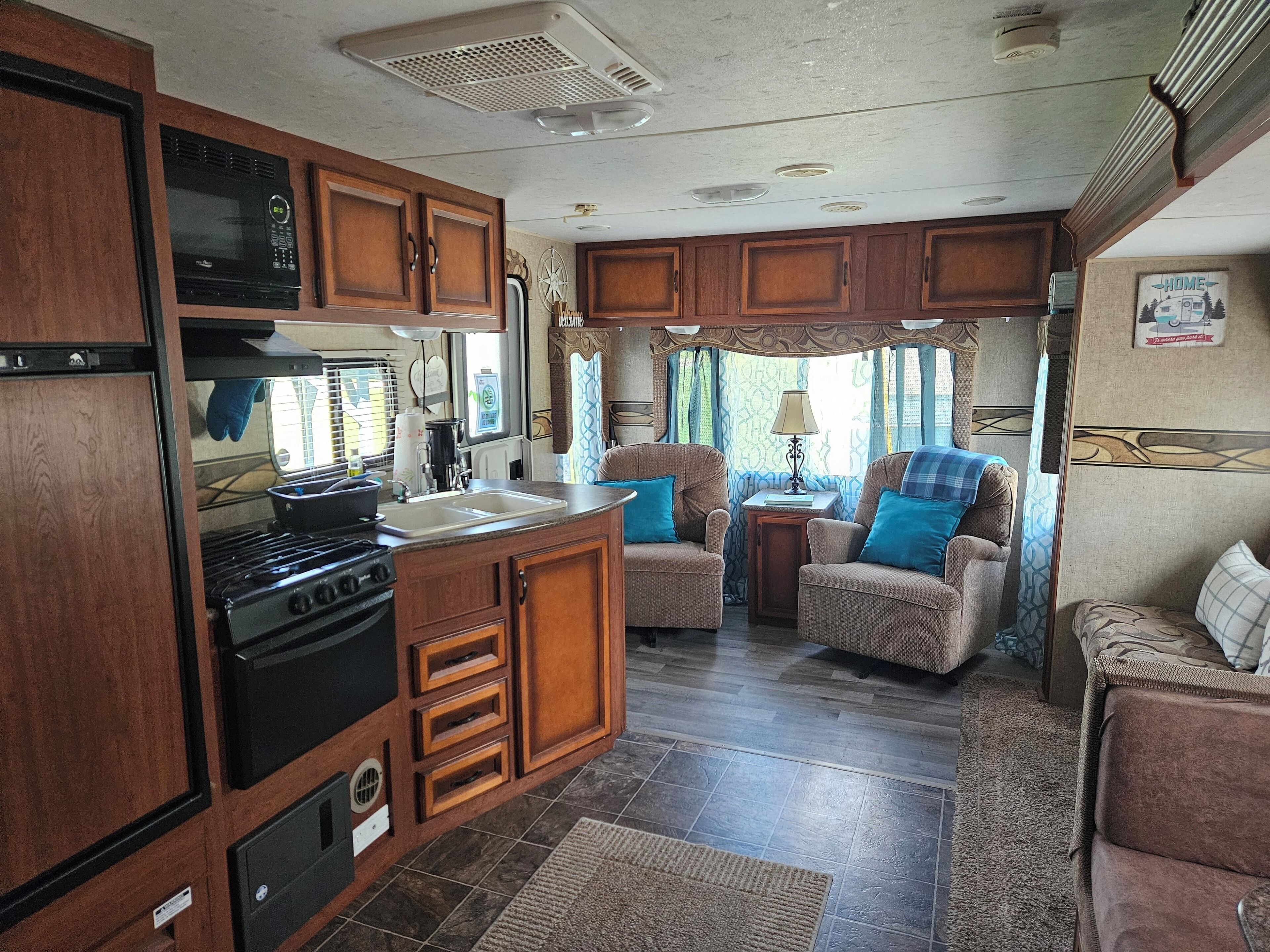 A compact RV kitchen with a stove, sink, and wooden cabinets.