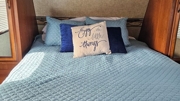 Ein Bett mit einer gesteppten, blauen Bettdecke, zwei Kissen und einem Kopfteil mit Holzpaneelen und integrierter Beleuchtung.