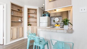 A modern kitchen with wooden cabinets, a built-in microwave, and a small island with bar stools. - Ocean View Condo (Corpus Christi)