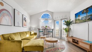 A living room with a yellow sofa, a round wooden coffee table, and a TV on the wall. - Ocean View Condo (Corpus Christi)
