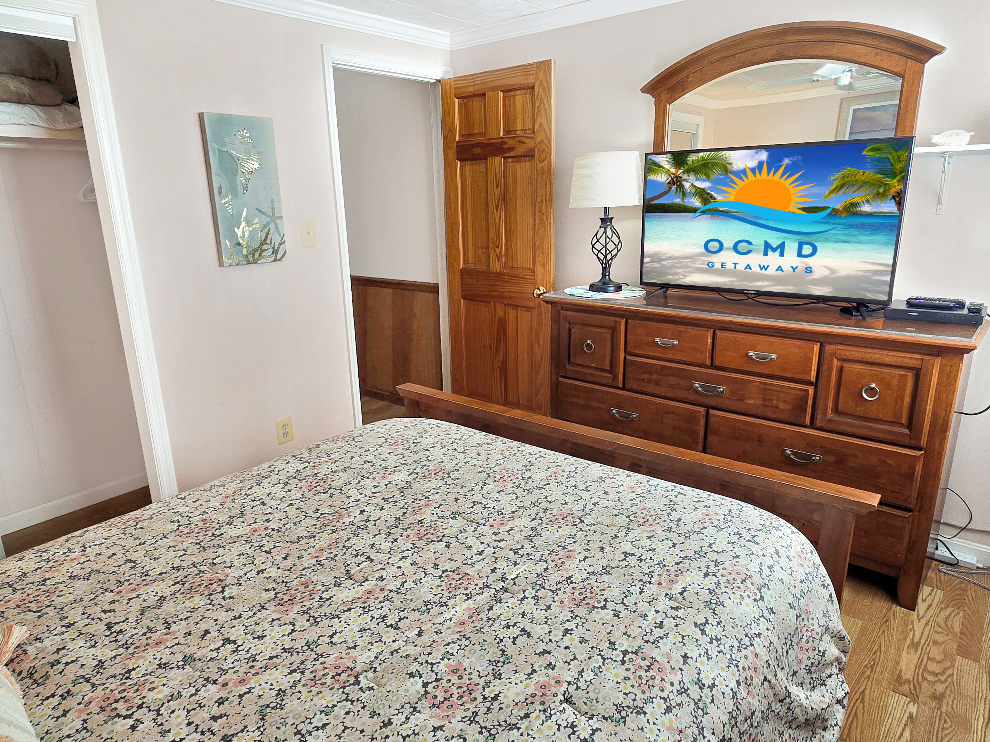 A bedroom with a bed, wooden dresser, TV, and a painting.
