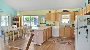 Une cuisine avec des meubles de rangement en bois, un réfrigérateur blanc et un coin repas comprenant une table et des chaises.
