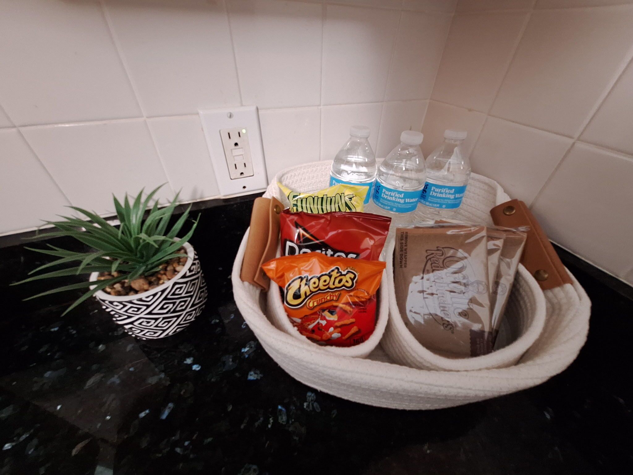 A kitchen counter with a potted plant, a basket containing snacks, water bottles, and a knife.