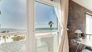 Ein Zimmer mit großem Fenster mit Blick auf den Strand, einem Schreibtisch mit Lampe und einem Globus darauf.