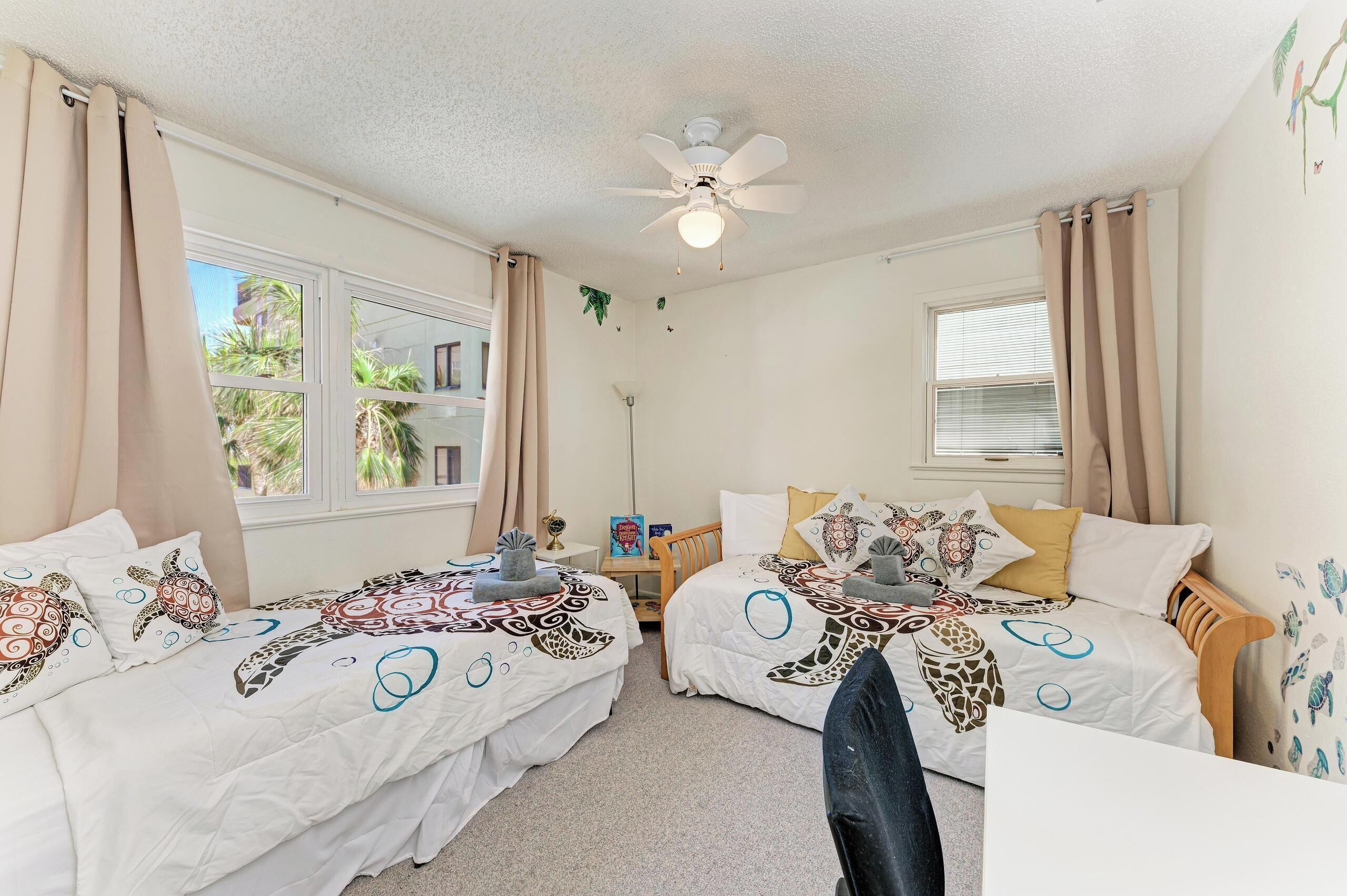Une chambre avec deux lits, un ventilateur de plafond et une fenêtre avec des rideaux.