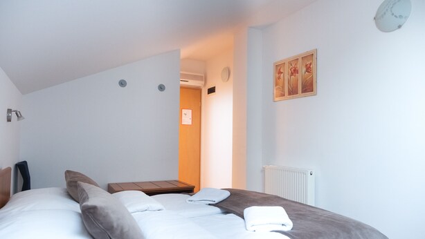 A bedroom with a bed, pillows, a nightstand, a wall clock, and a radiator. - Romantic attic 1/2 room (Izola)