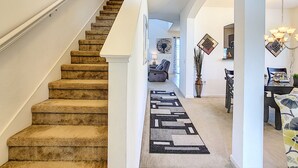 Una escalera con peldaños alfombrados que lleva a una sala de estar con una mesa de comedor y sillas.