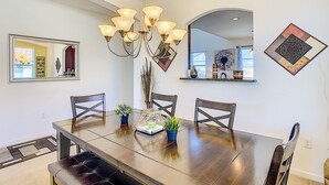 Un comedor con una gran mesa de madera, cuatro sillas, una araña y decoración en la pared.