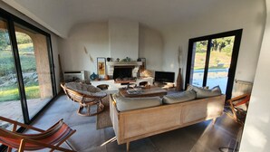 A spacious living room with a fireplace, comfortable seating, and large windows offering a view of the outdoors. - Magnificent pool villa between sea and mountains (Céret)