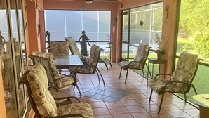 Une terrasse ensoleillée avec un sol carrelé, des sièges d’extérieur et un ventilateur de plafond.