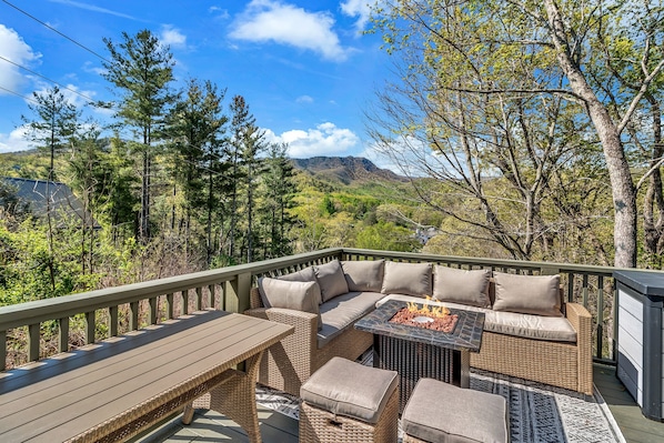 A deck with wicker furniture, a fire pit, and a view of a mountainous landscape.