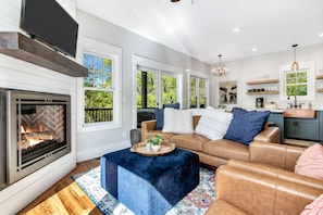 A modern living room with a fireplace, leather sofa, and a kitchen area with a countertop and pendant lights.