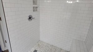 Eine Dusche mit weißen Fliesen an den Wänden und einem Mosaikboden.