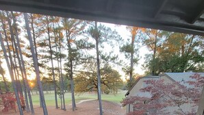 Ein überdachter Außenbereich mit Blick auf einen Golfplatz, einem Holzzaun und einem Blumentopf auf einem Tisch.