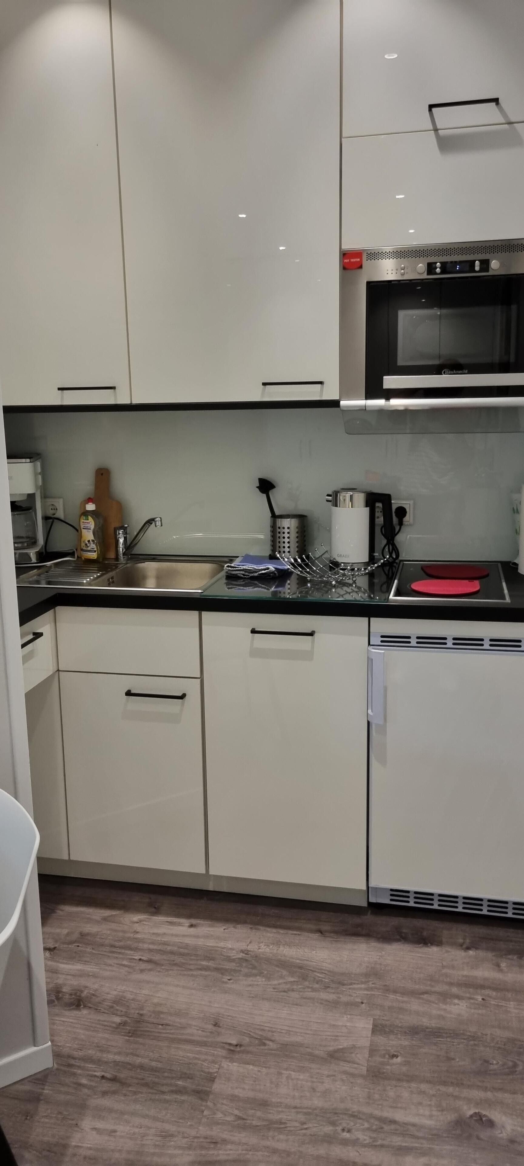 Een moderne keuken met witte kasten, een roestvrijstalen spoelbak, een magnetron en een vaatwasser.