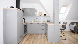 Eine moderne Küche mit grauen Schränken, einer Holz Arbeitsplatte und einem eingebauten Ofen. Ein Essbereich mit Tisch und Stühlen lädt zum Verweilen ein, und ein Fenster sorgt für natürliches Licht.