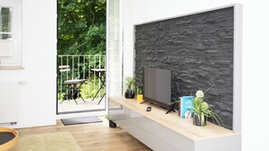 Ein modernes Wohnzimmer mit Steinwand, Flachbildfernseher und einem Holzkonsolentisch mit Pflanzen und Büchern.