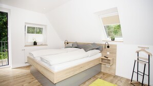 Ein modernes Schlafzimmer mit einem großen Bett, einem kleinen Nachttisch, einer Nachttischlampe, einem Fenster mit Blick und einer Balkontür.